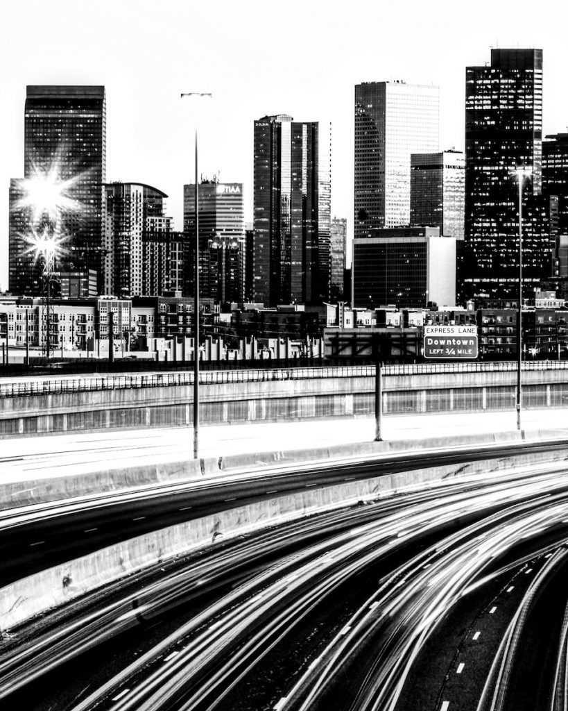 Black and white photo of the downtown skyline with passing traffic in the foreground