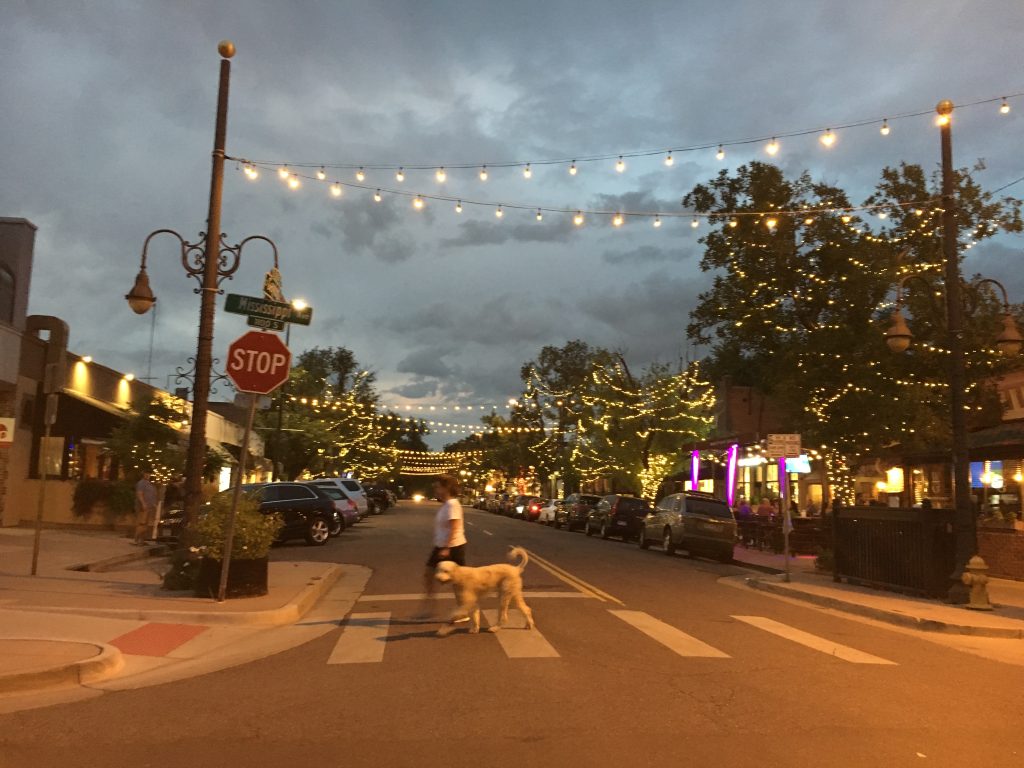 photo taken from the intersection at dusk. White cafe lights line the block.